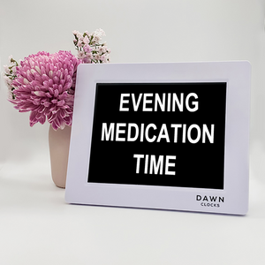 Original Dawn Clock shown on a table with the "Evening medication time" reminder on the screen. This is ideal for all ages and proved essential for NDIS participants, people living with Dementia, people living with a disability and seniors.